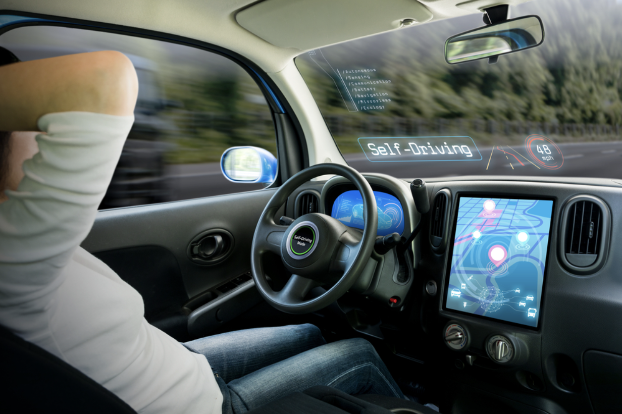 A woman in the driver's seat of a self-driving car, with a tablet placed on the dashboard.