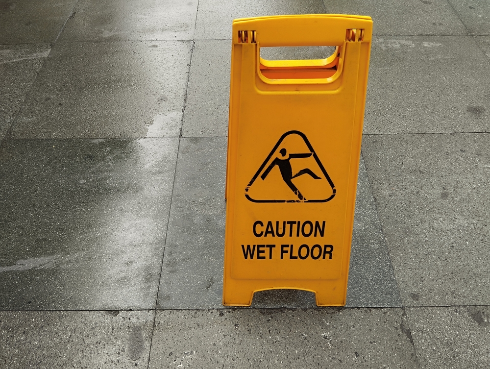 A bright yellow "CAUTION WET FLOOR" sign with a slipping hazard icon placed on a wet, tiled floor. Essential for safety and preventing accidents in public or commercial spaces.