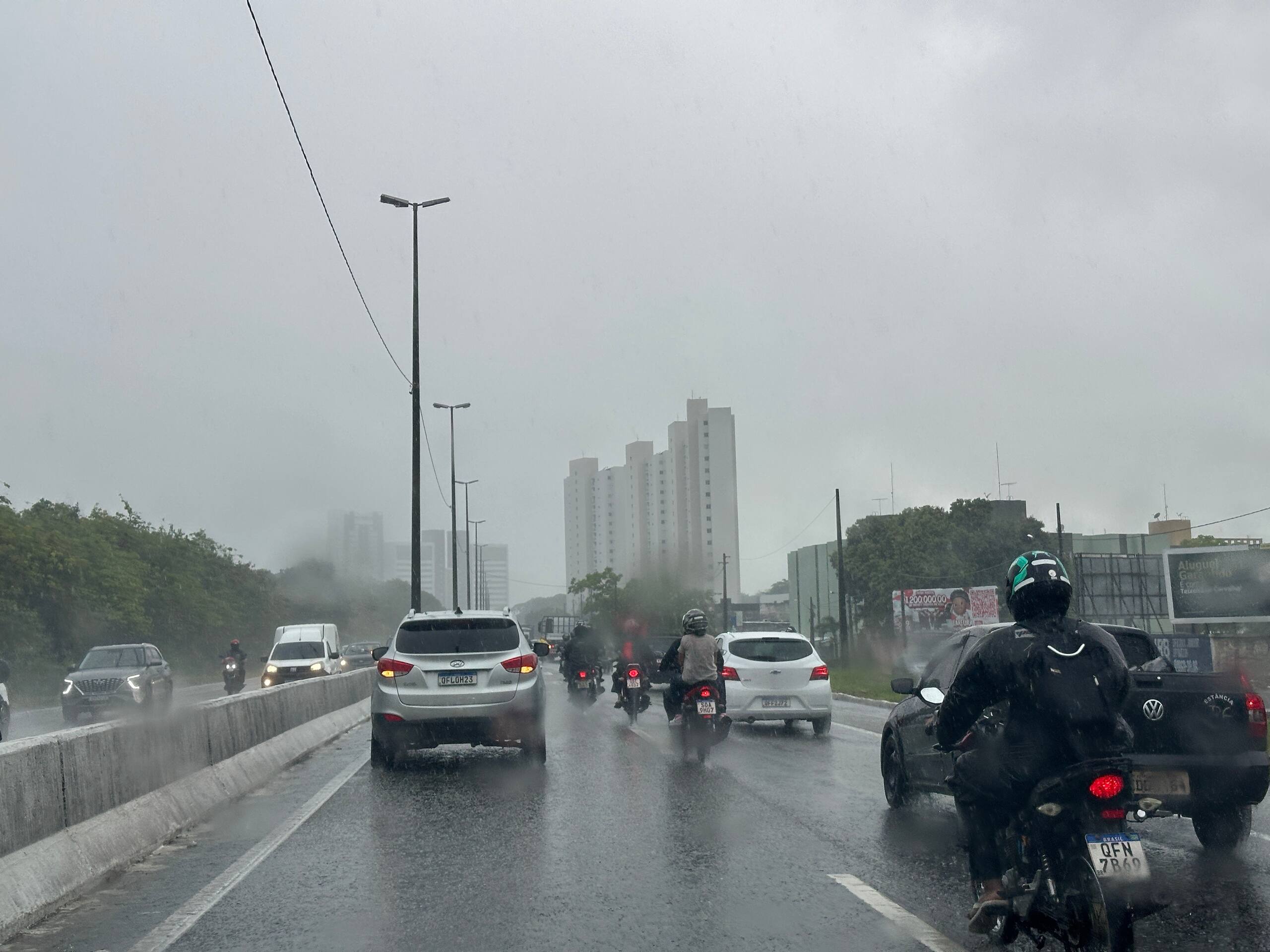 Motorcyclists lane filtering through stopped traffic on a busy Provo road during rain.