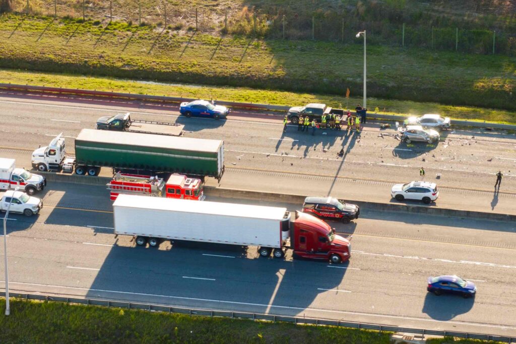 Aerial view of multi-vehicle highway crash with semi-truck and emergency responders, representing potential claims for injuries caused by falling cargo in Midvale.