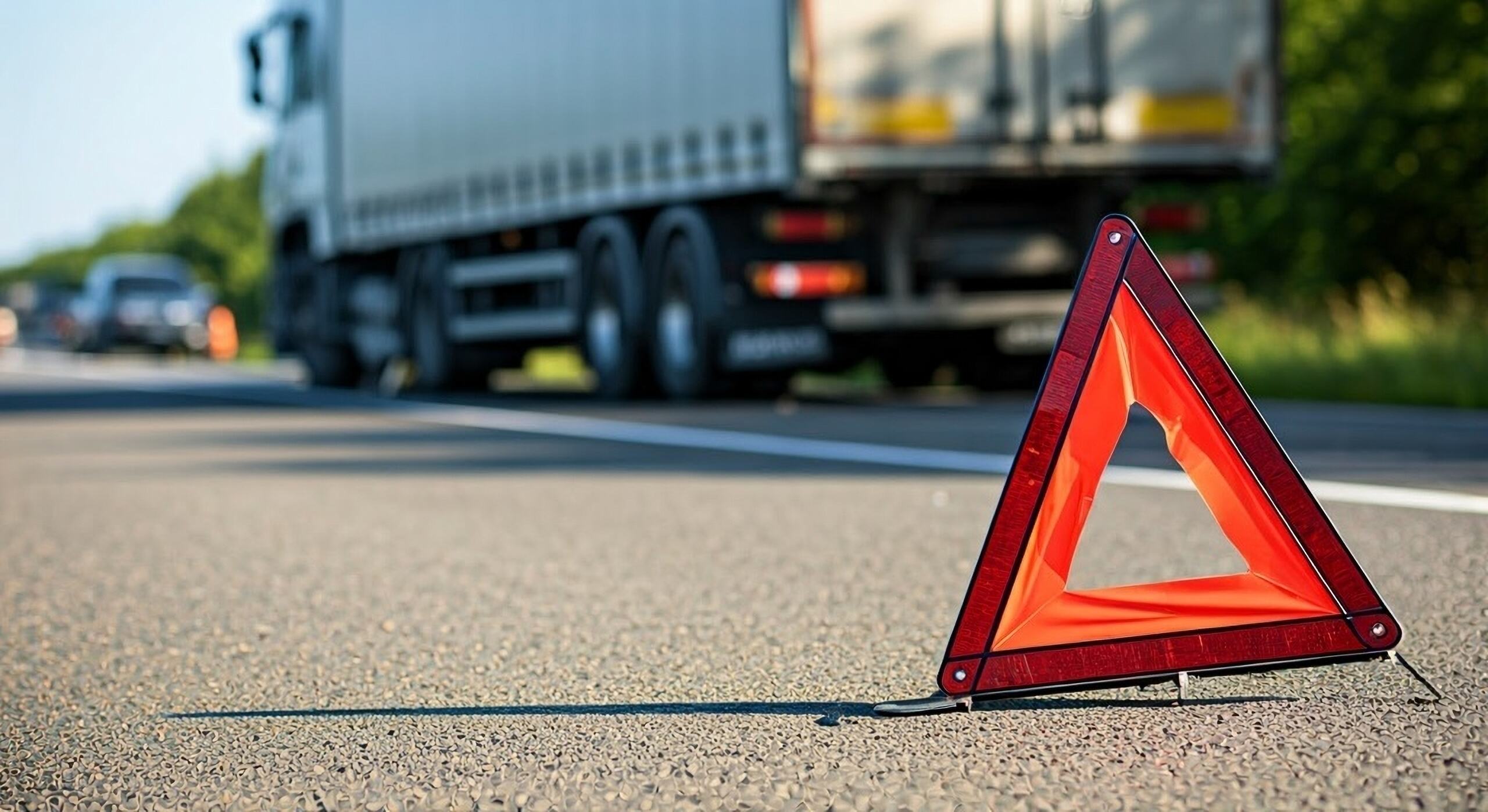 Roadside emergency warning triangle in front of a commercial truck, representing Midvale truck accident injuries and early insurance settlement pressure.