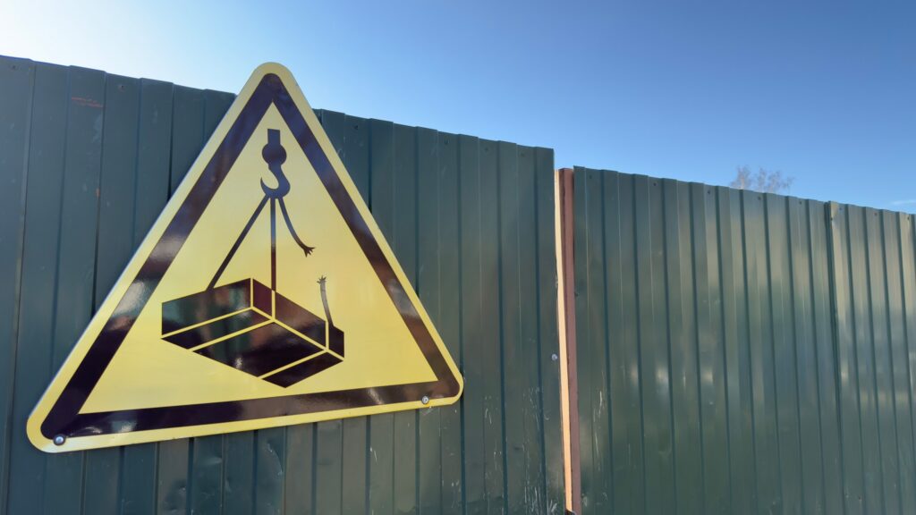 Safety signage in Provo warning of falling loads and crane accidents at a construction site.