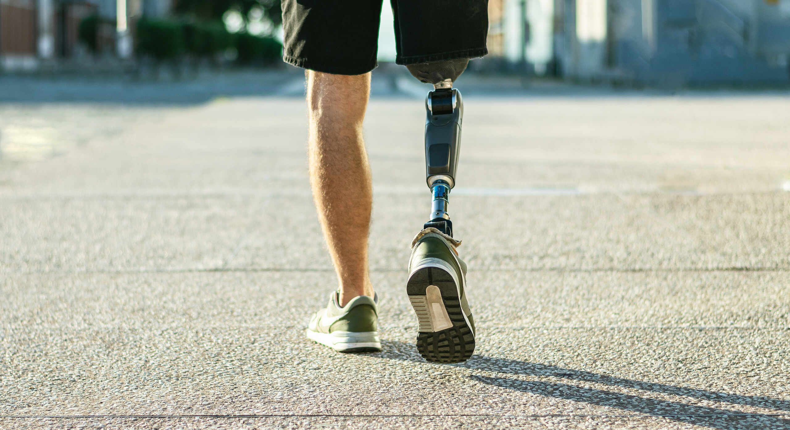 Rear view of a person wearing an advanced prosthetic leg while walking outdoors on a paved pathway.