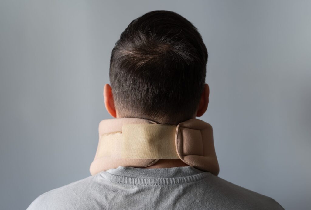 A rear view of a person wearing a tan medical neck brace to stabilize the cervical spine after an accident.