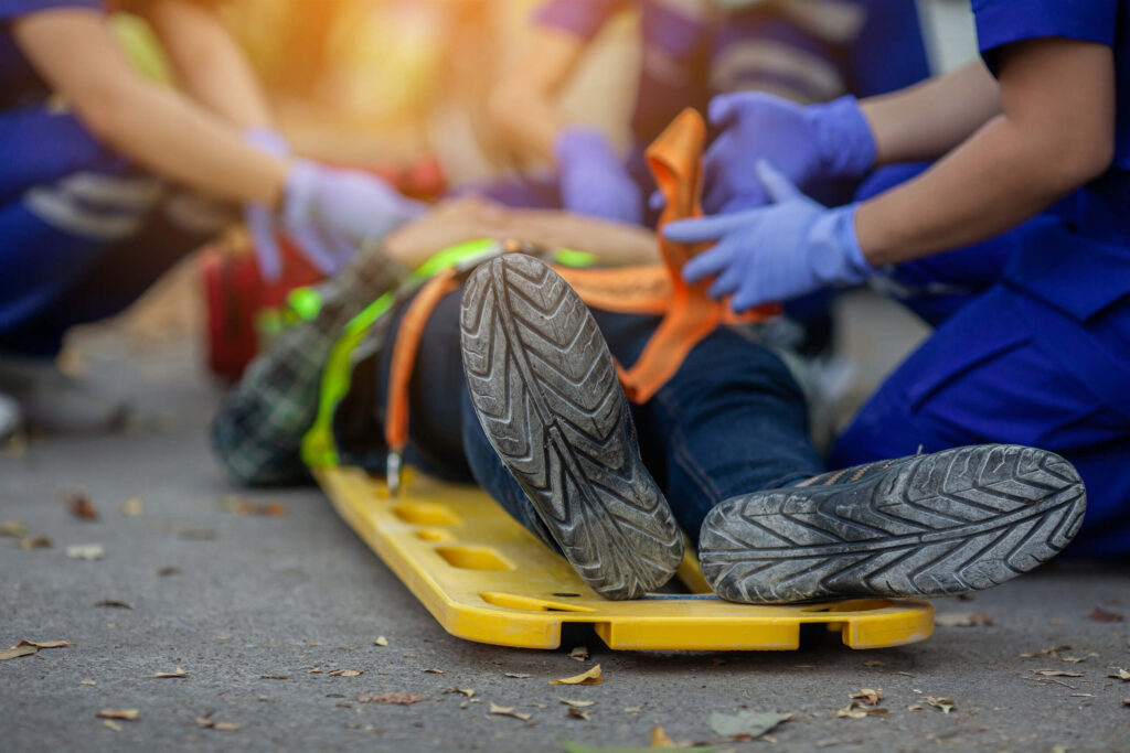Emergency responders in blue uniforms and gloves secure an injured person onto a yellow medical stretcher at an accident scene.