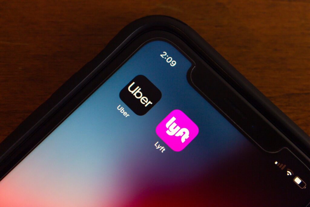 A close-up view of a smartphone screen displaying the Uber and Lyft mobile app icons on a dark background.