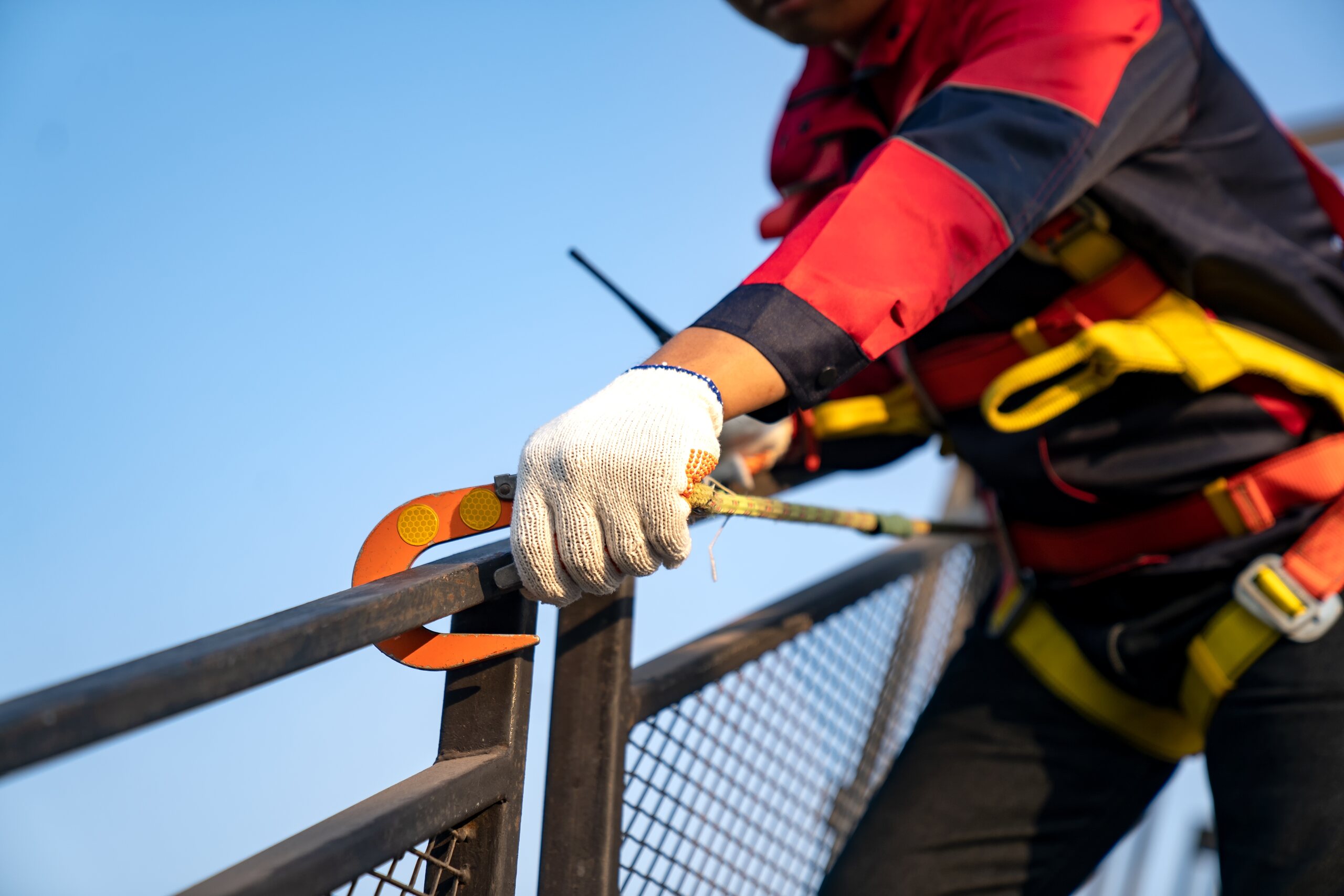 A construction worker wearing a yellow safety vest and hard hat stands in front of a heavy excavating machine at a work site.