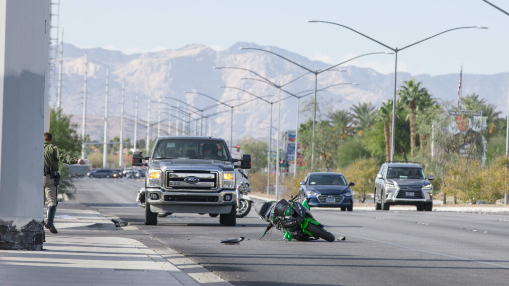 A green and black sport motorcycle lies crashed on its side in the middle of a multi-lane city street with traffic and a police officer nearby, illustrating traffic regulations covered in a guide to Utah’s motorcycle laws.