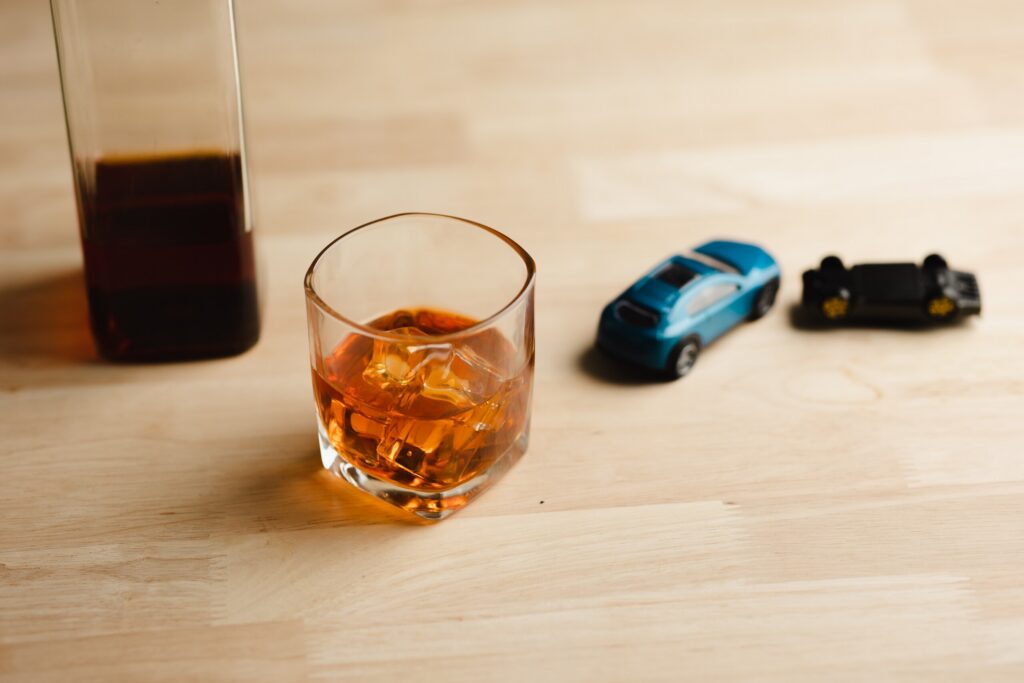 A glass of liquor with ice sitting next to tiny toy cars on a wooden table, symbolizing drunk driving dangers handled by Salt Lake City DUI Accident Lawyers.