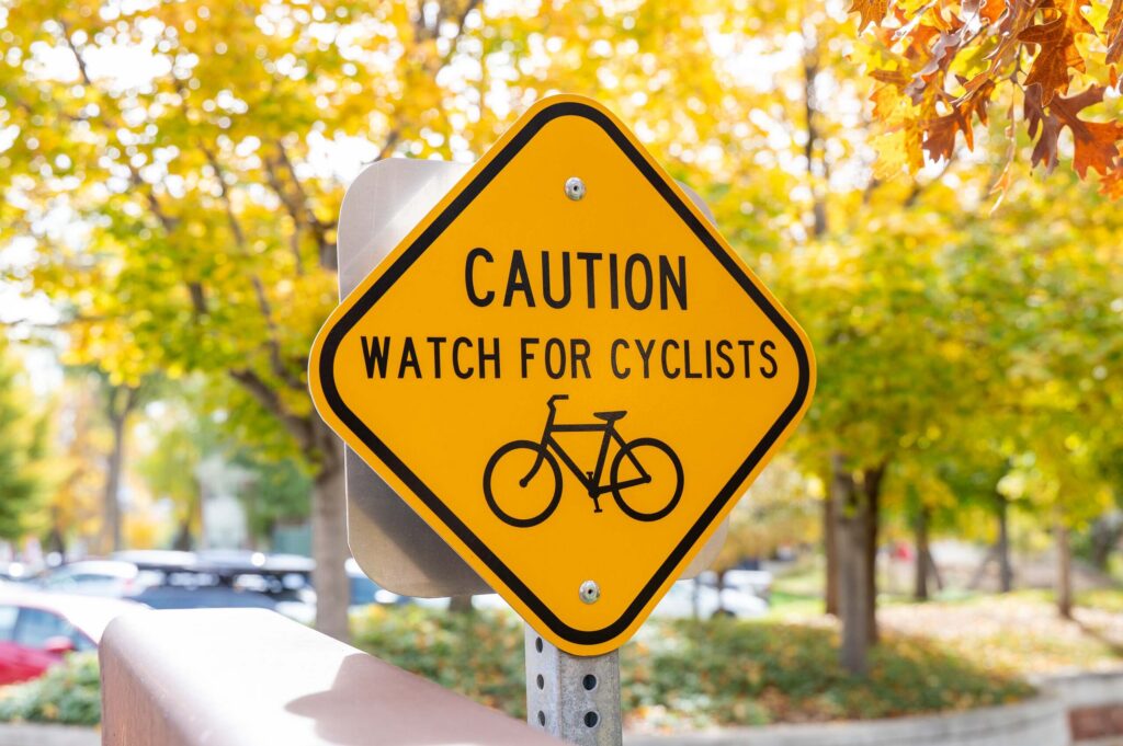 A yellow diamond road sign reading "CAUTION WATCH FOR CYCLISTS" with a bicycle icon, emphasizing traffic safety concepts for Utah Bicycle Accident Lawyers.