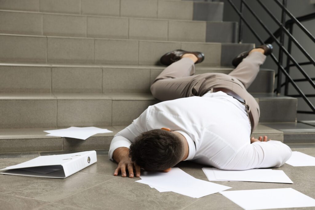 A man lying fallen at the bottom of a staircase with scattered papers represents injury cases managed by Rock Springs Premises Liability Lawyers.