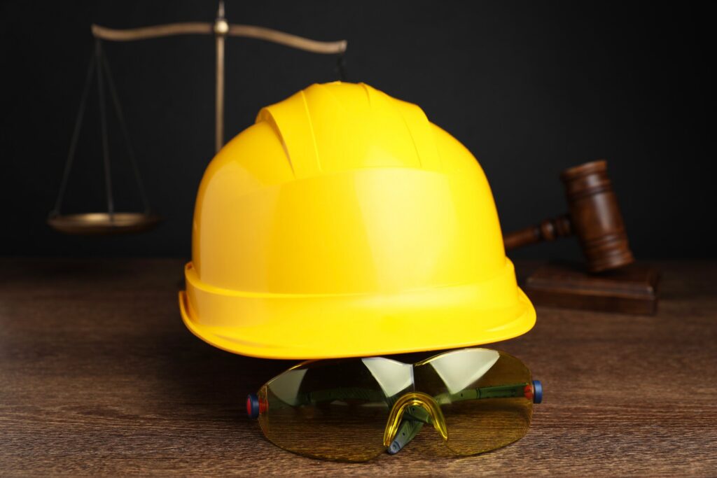 A yellow hard hat safety glasses scale of justice and gavel represent claims handled by Spokane Construction Accident Lawyers.