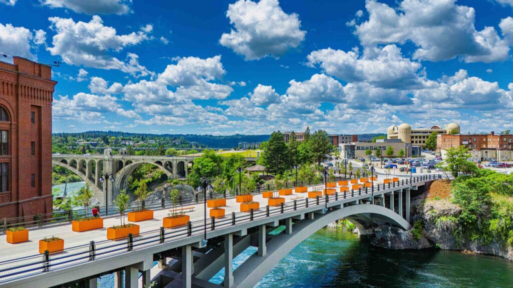 A scenic view of a bridge lined with orange planters crossing the Spokane River highlights the area served by Spokane Construction Accident Lawyers.